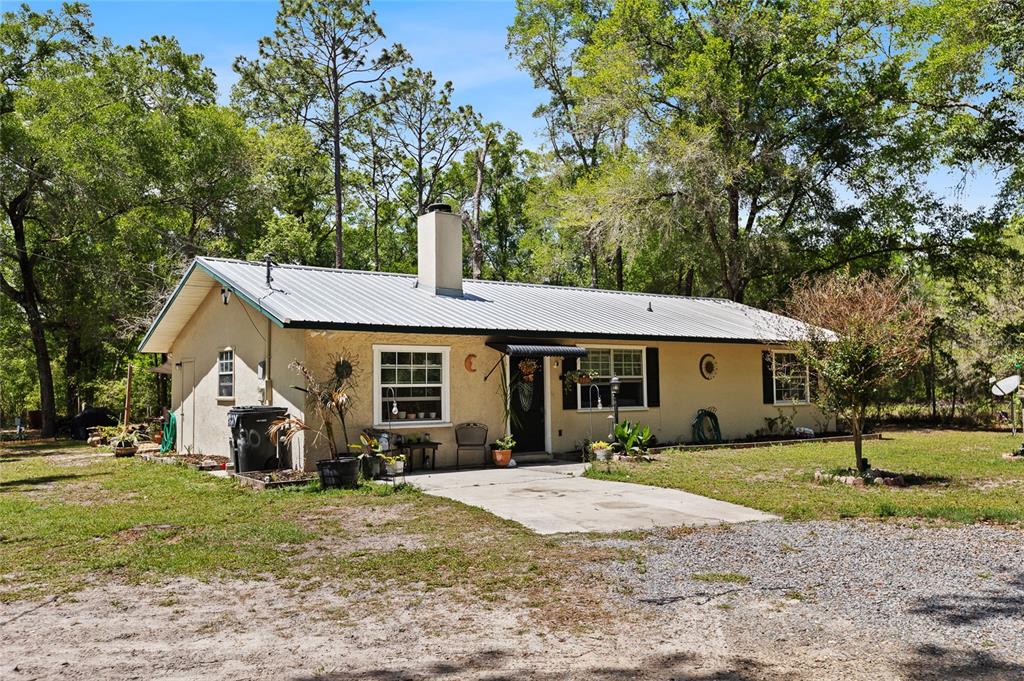 A single-story house with a metal roof and stucco exterior sits in a wooded lot — 5420 E GWENDOLYN PATH, INVERNESS, FL