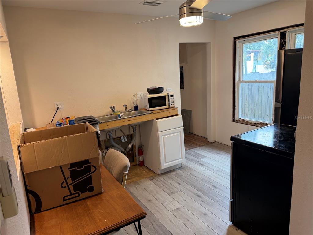 A kitchen features a sink with exposed plumbing, a microwave, and light wood-look flooring — 618 15TH STREET N, ST PETERSBURG, FL