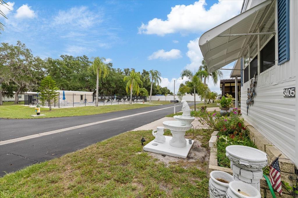 A white mobile home exterior features a tiered fountain and a nearby community swimming pool — 3405 FLORENCE DRIVE, ELLENTON, FL