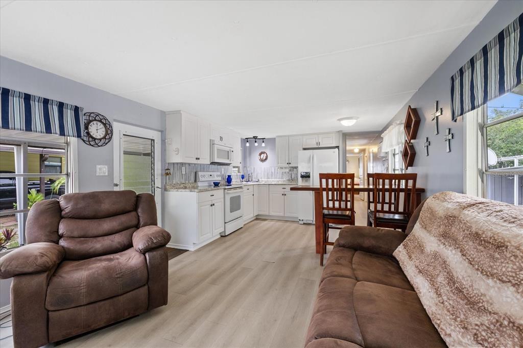 An open-concept living room and kitchen featuring white cabinetry, wood-look flooring, and brown furniture — 3405 FLORENCE DRIVE, ELLENTON, FL
