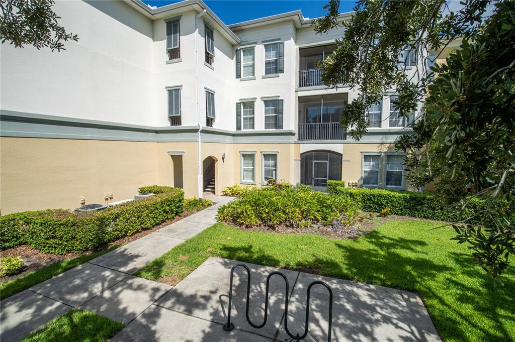 A multi-story apartment building exterior features a sidewalk, bike rack, and landscaped green space — 8180 BOAT HOOK LOOP UNIT 102, WINDERMERE, FL