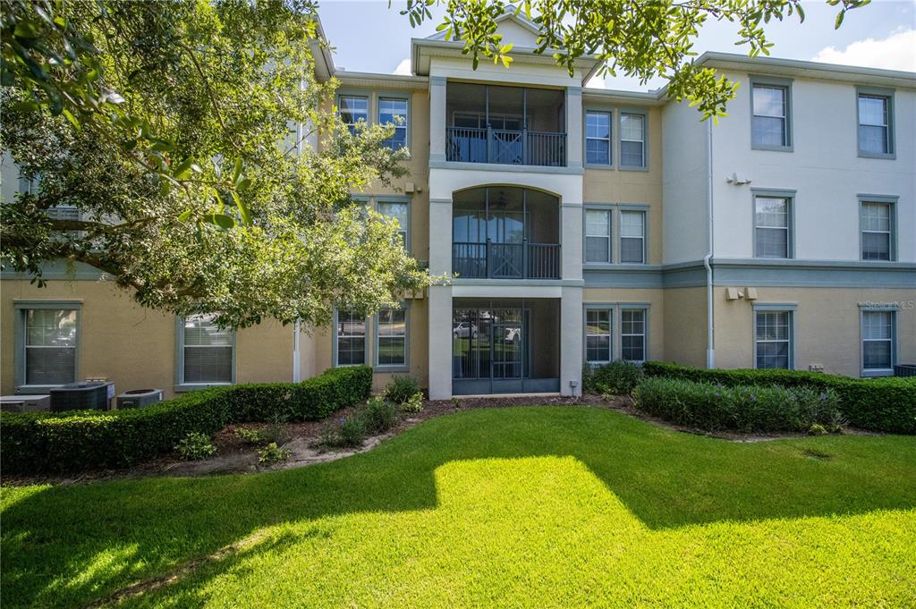 A three-story apartment building features screened balconies, tan stucco walls, and a landscaped lawn — 8180 BOAT HOOK LOOP UNIT 102, WINDERMERE, FL