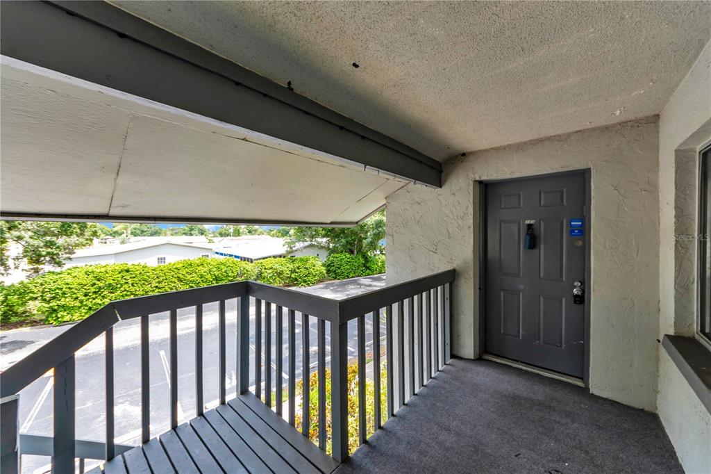An exterior view of an apartment balcony with a gray door and wooden railing — 11201 122ND AVENUE UNIT 146, LARGO, FL