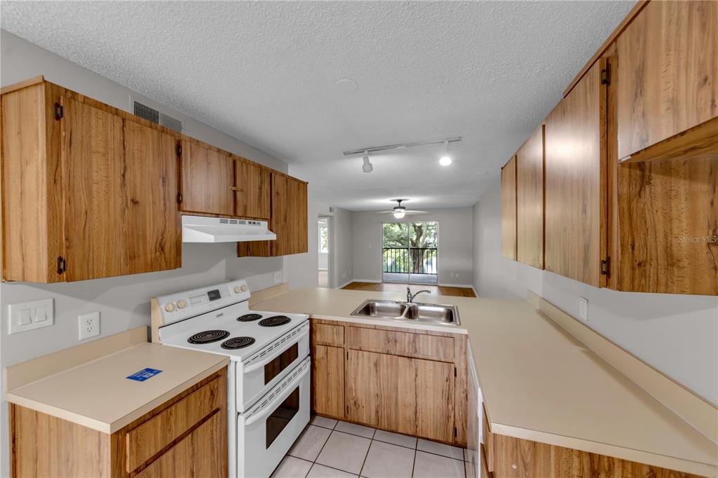 A kitchen features wood-grain cabinets, white appliances, beige countertops, and tile flooring — 11201 122ND AVENUE UNIT 146, LARGO, FL