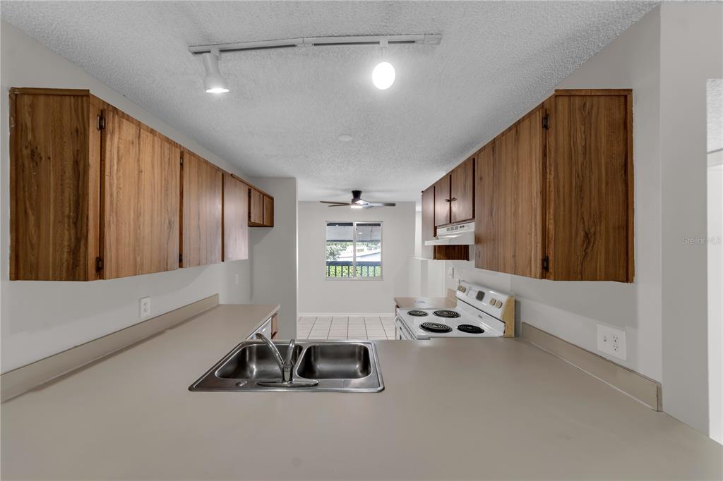 A kitchen features wood cabinets, a double-basin sink, and a view into the dining area — 11201 122ND AVENUE UNIT 146, LARGO, FL