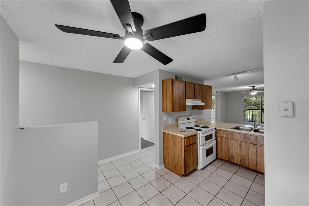 A kitchen with wood cabinets, white appliances, and tile flooring opens to a dining area — 11201 122ND AVENUE UNIT 146, LARGO, FL