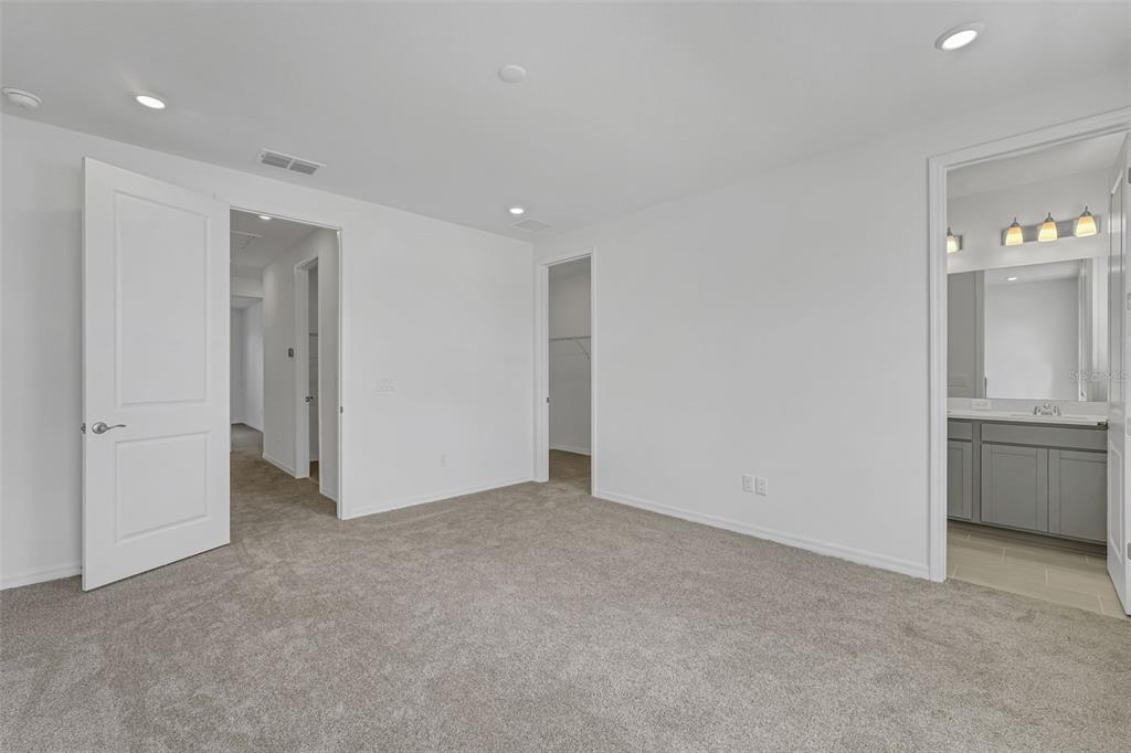 An empty bedroom with gray carpet, white walls, recessed lighting, and an attached bathroom — 31789 KESTREL CALLING DRIVE, SAN ANTONIO, FL