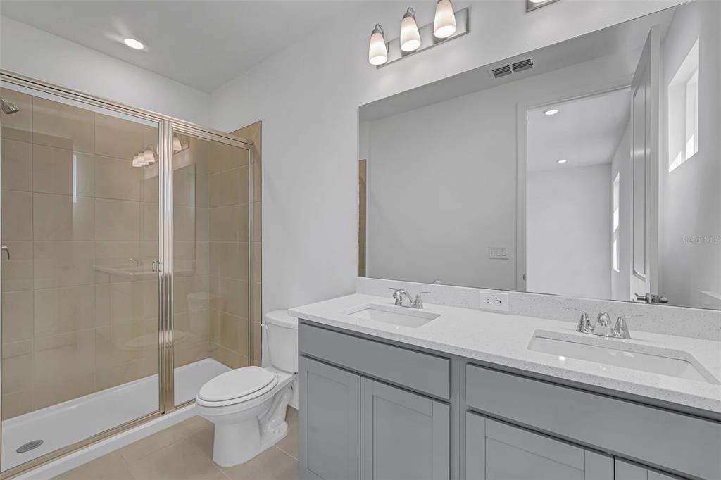 A bathroom features a double vanity with gray cabinets, a large mirror, and a glass shower — 31789 KESTREL CALLING DRIVE, SAN ANTONIO, FL