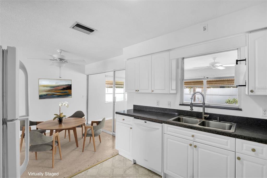 A kitchen with white cabinets and dark countertops opens to a dining area with seating — 2301 WHITMAN STREET, CLEARWATER, FL
