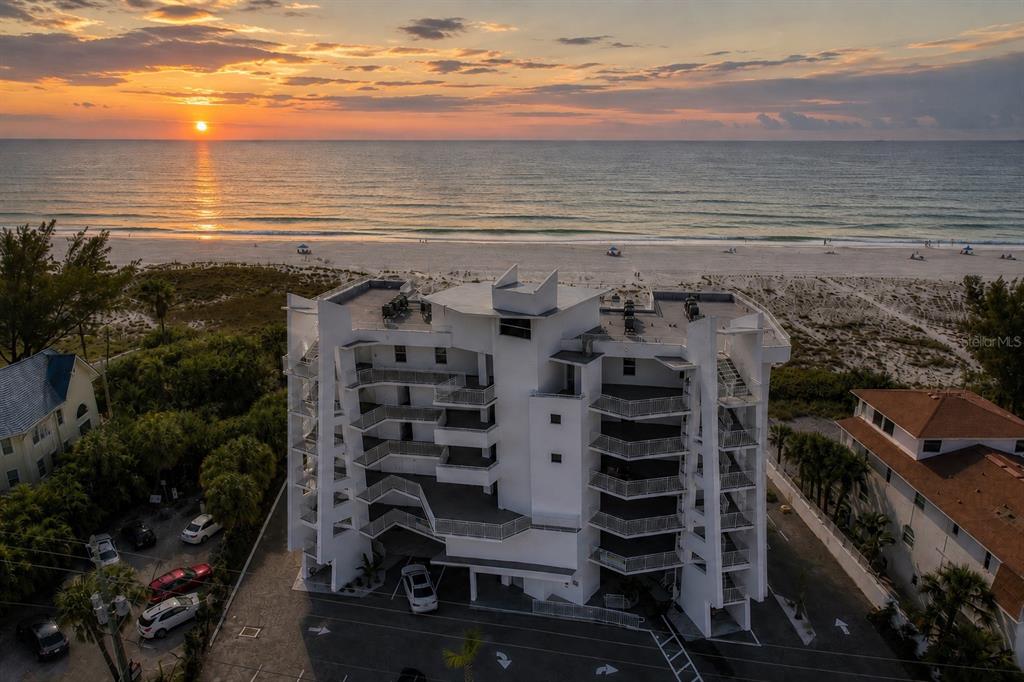 An aerial view of a white multi-story beachfront condominium building at sunset — 10116 GULF BOULEVARD UNIT 201W, TREASURE ISLAND, FL