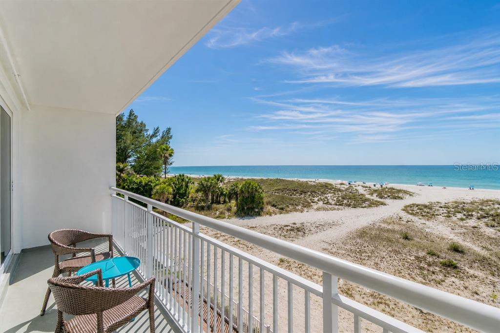 A balcony with two wicker chairs overlooks a sandy beach and the ocean — 10116 GULF BOULEVARD UNIT 201W, TREASURE ISLAND, FL