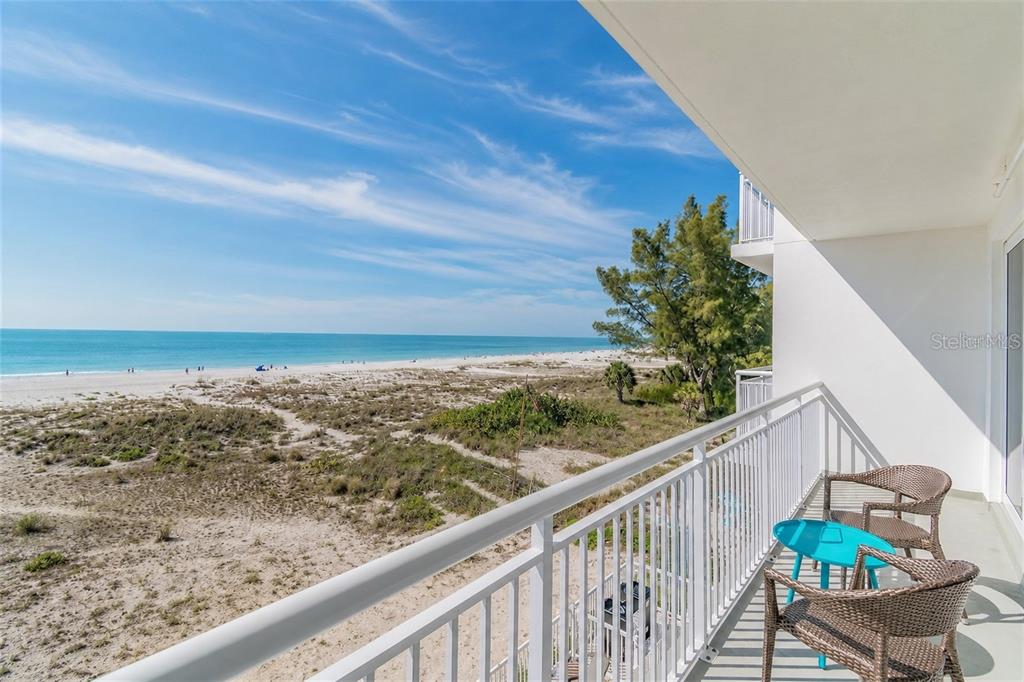 A balcony with two chairs and a small table overlooks a sandy beach and ocean — 10116 GULF BOULEVARD UNIT 201W, TREASURE ISLAND, FL