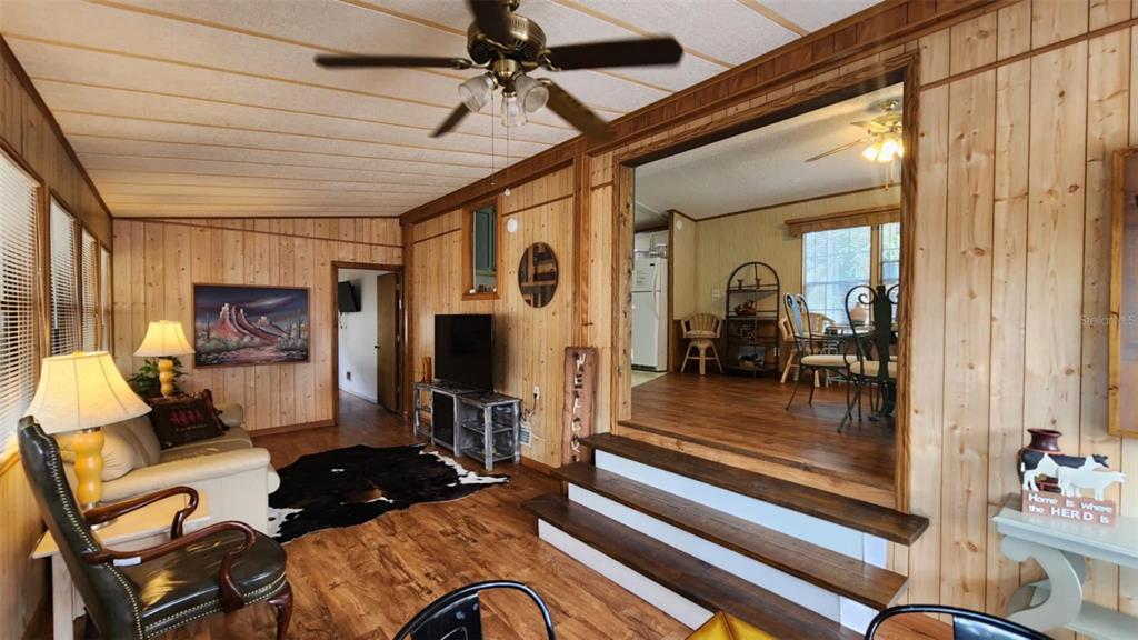 A living room with wood-paneled walls leads up two steps into a dining area — 9 LONG HAMMOCK DRIVE, RIVER RANCH, FL