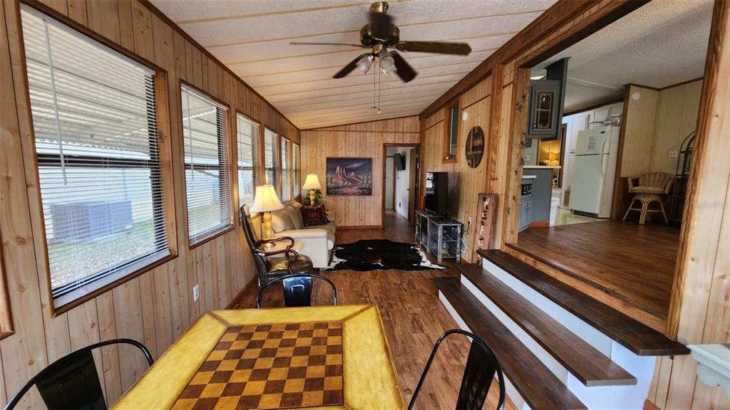 A sunroom with wood-paneled walls and a checkerboard table leads to a raised kitchen area — 9 LONG HAMMOCK DRIVE, RIVER RANCH, FL