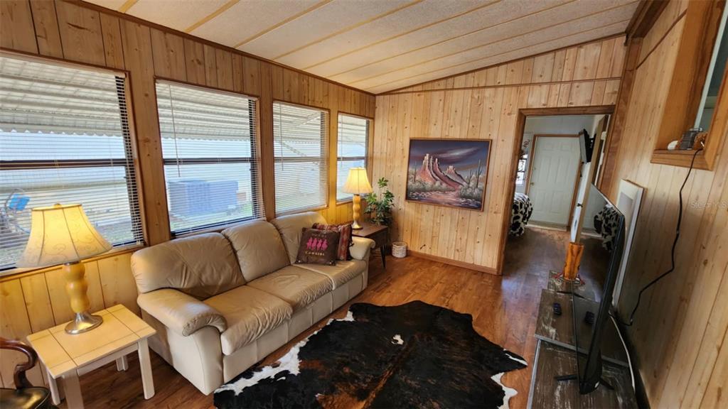 A living room features wood-paneled walls, a leather sofa, a cowhide rug, and large windows — 9 LONG HAMMOCK DRIVE, RIVER RANCH, FL