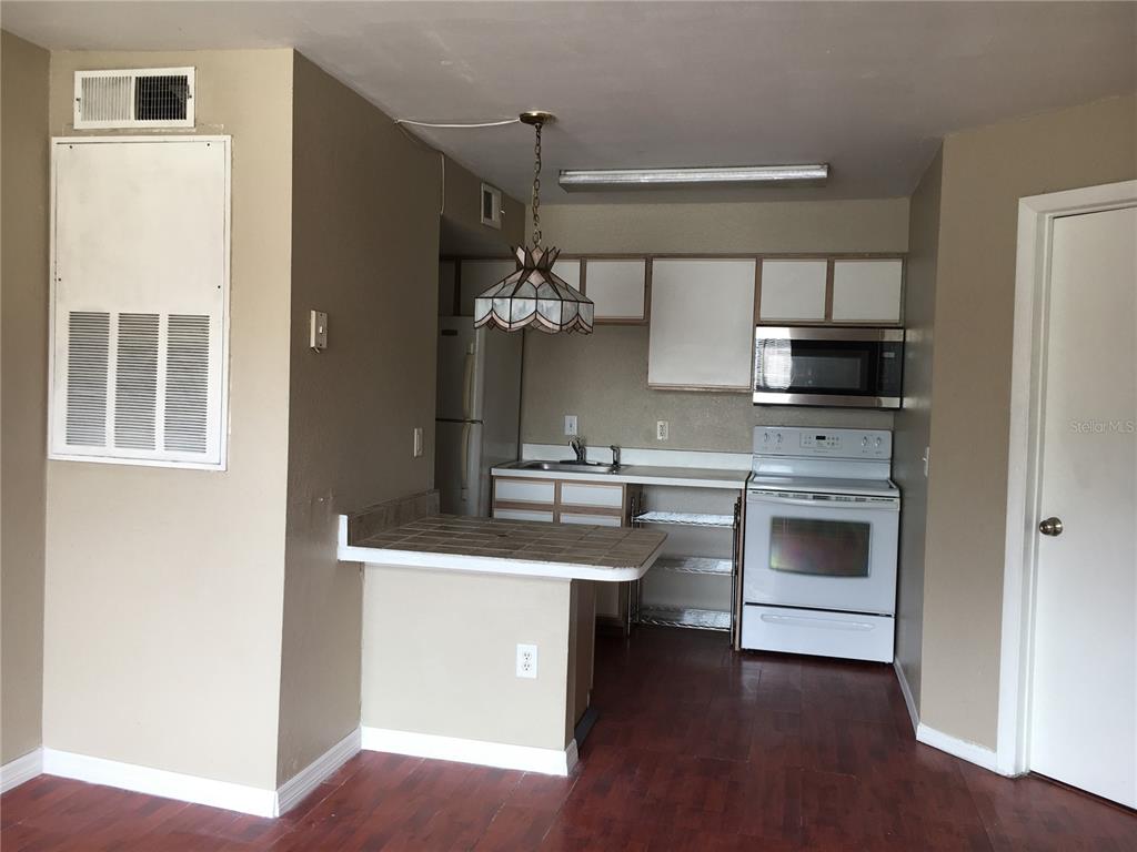 A kitchen features white cabinets, a white stove, a tiled breakfast bar, and wood flooring — 2200 KEY WEST COURT UNIT 723, KISSIMMEE, FL