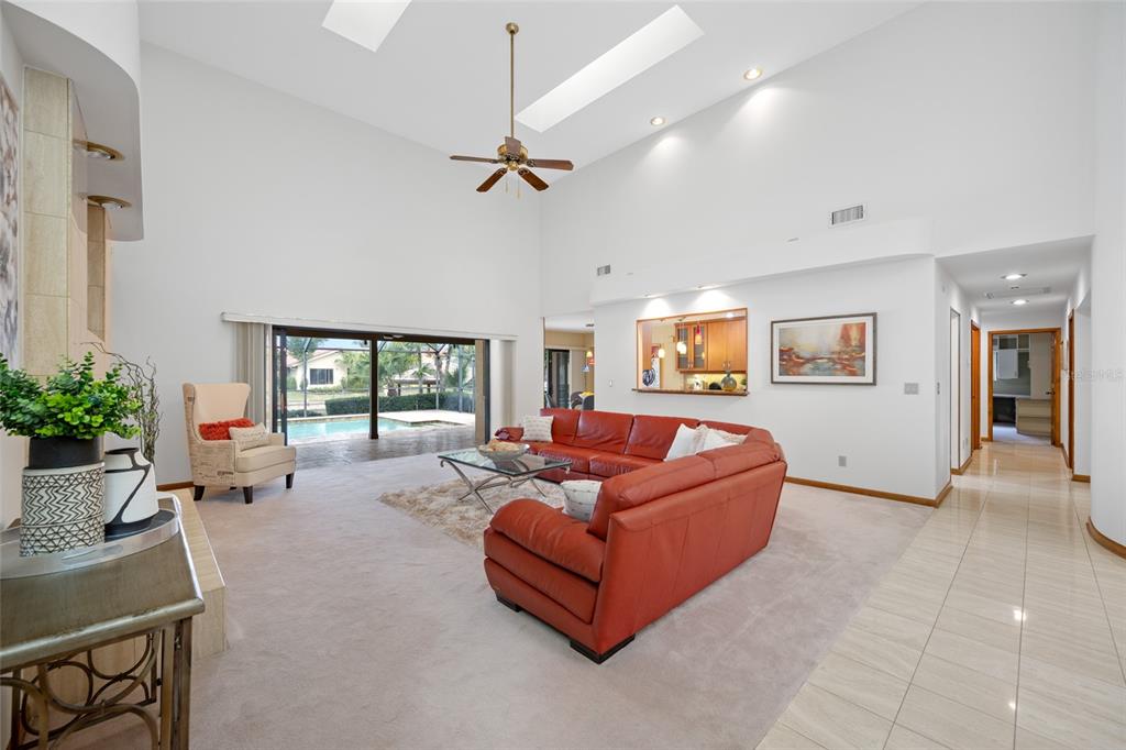 A spacious living room features a red sectional sofa, vaulted ceilings, skylights, and pool views — 9807 COMPASS POINT WAY, TAMPA, FL