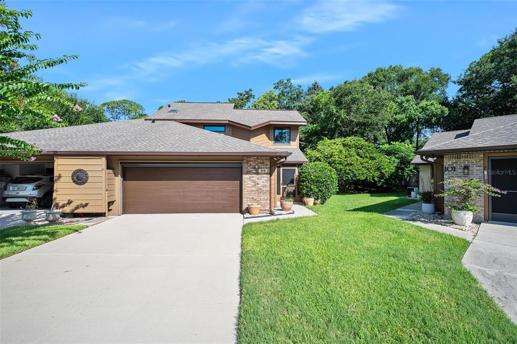An exterior view of a two-story residential building with a brown garage and green lawn — 99 OLD BARN TRAIL, ORMOND BEACH, FL
