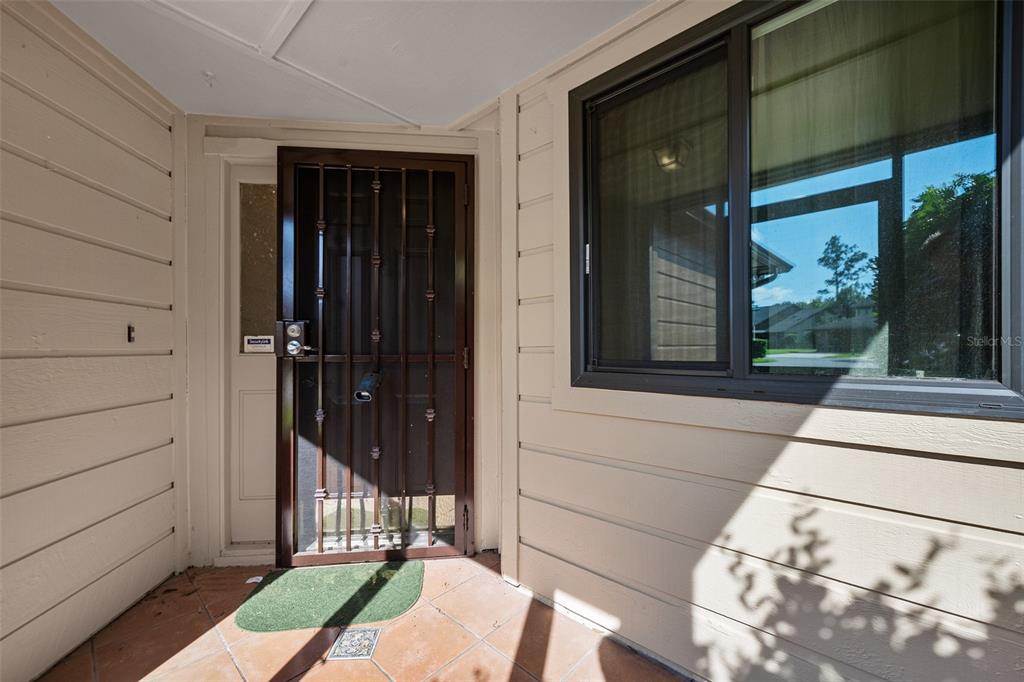 A front entryway features a brown security screen door, beige horizontal siding, and tiled flooring — 99 OLD BARN TRAIL, ORMOND BEACH, FL