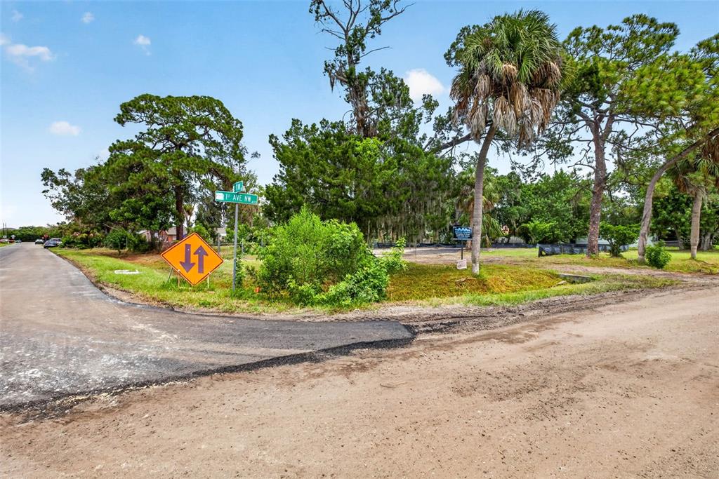 A dirt road meets a paved street corner near a vacant lot with trees — 409 1ST AVENUE NW, RUSKIN, FL