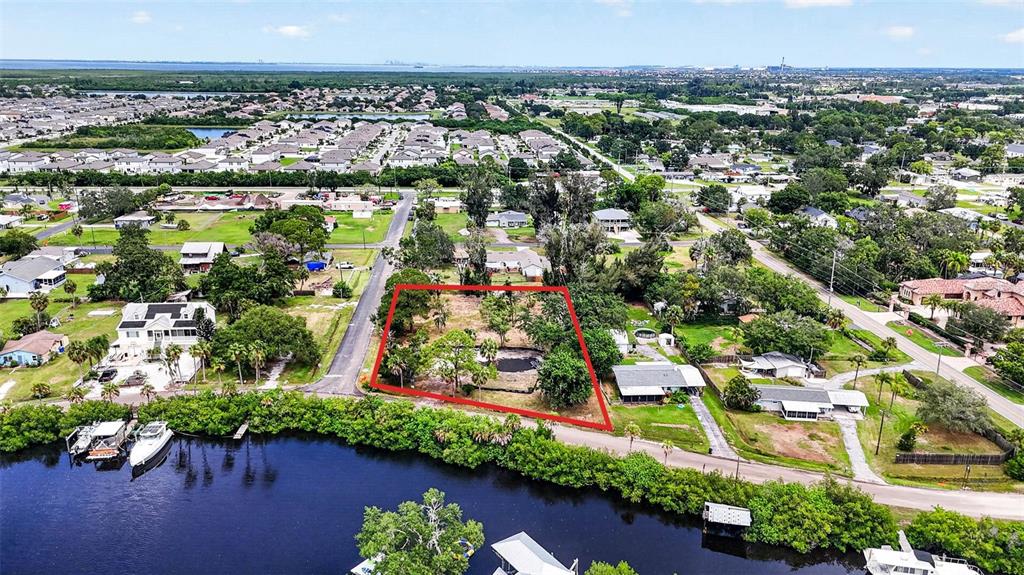 An aerial view shows a vacant, tree-filled lot outlined in red next to a waterfront — 409 1ST AVENUE NW, RUSKIN, FL