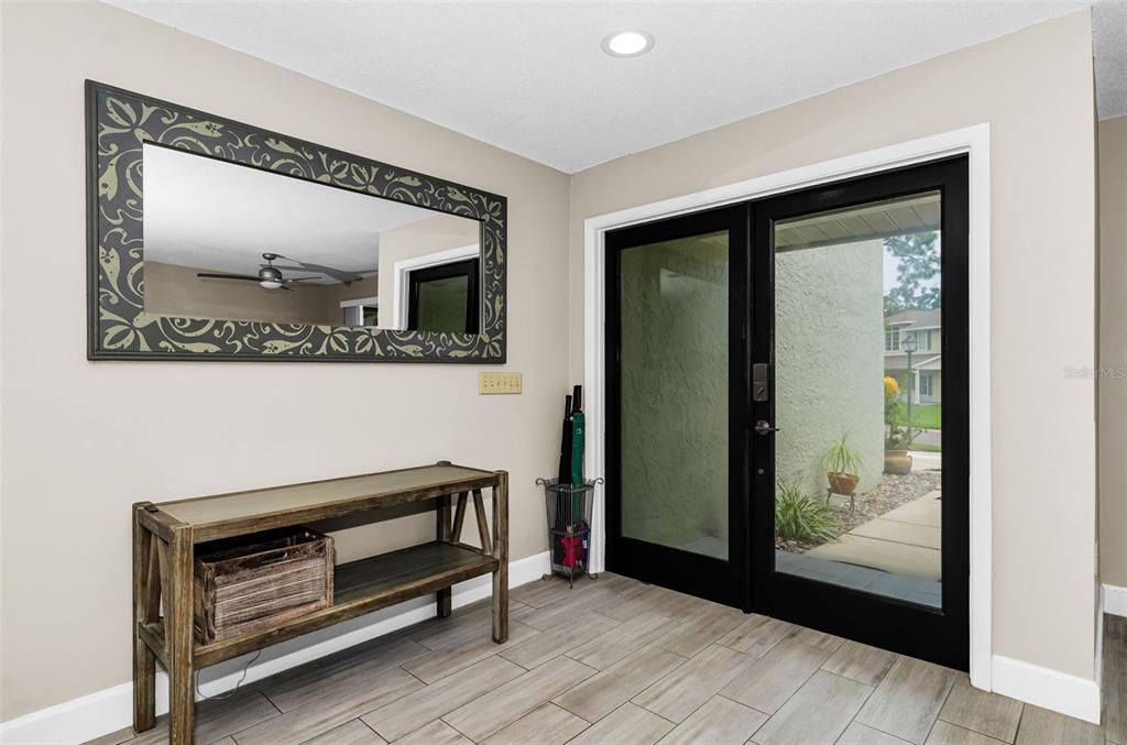 An entryway features a wooden console table, a decorative mirror, and black-framed glass double doors — 2063 BROOKSIDE DRIVE, SAFETY HARBOR, FL