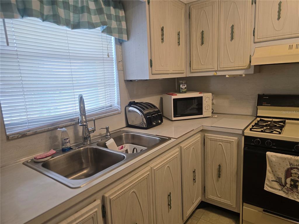 A kitchen features light wood cabinets, a double-basin sink, a microwave, and a gas stove — 5356 81ST STREET N UNIT 15, ST PETERSBURG, FL