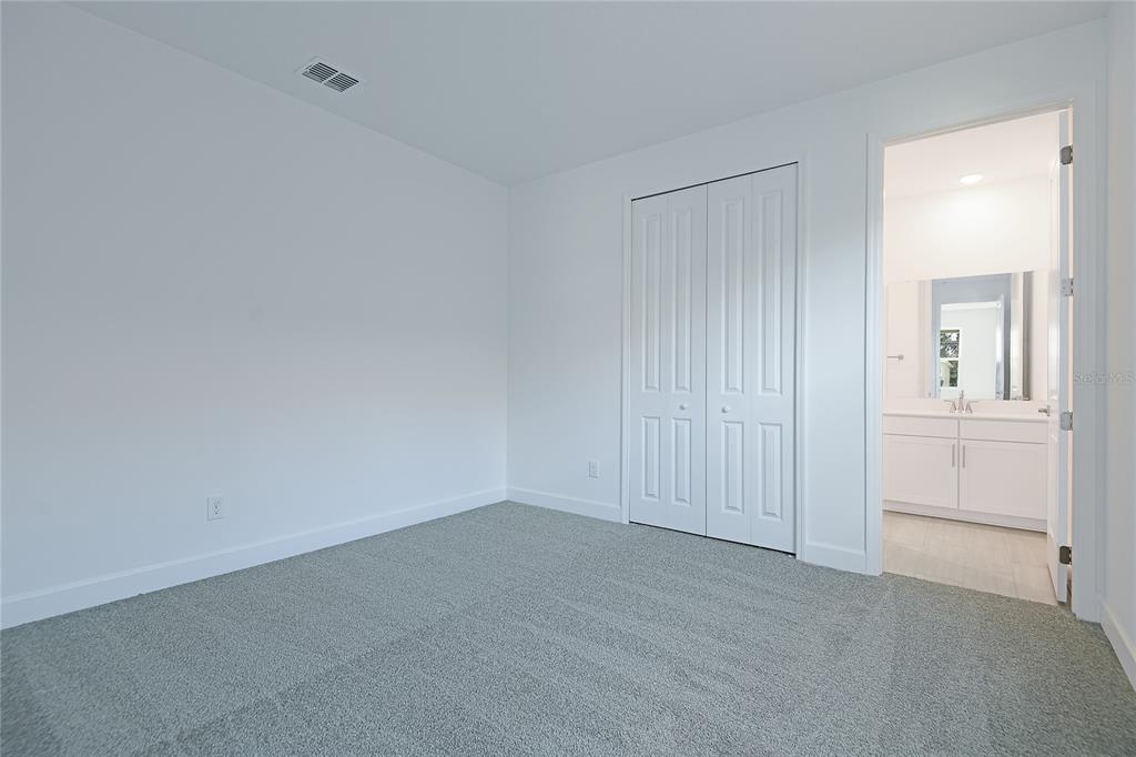 A bedroom with gray carpet, white walls, a closet, and an attached bathroom — 161 WATERSTONE LOOP, TAVARES, FL