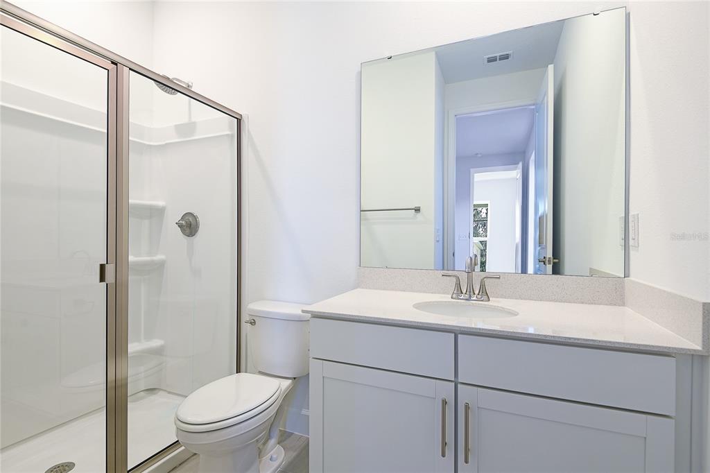 A bathroom features a glass-enclosed shower, a white toilet, and a vanity with a mirror — 161 WATERSTONE LOOP, TAVARES, FL