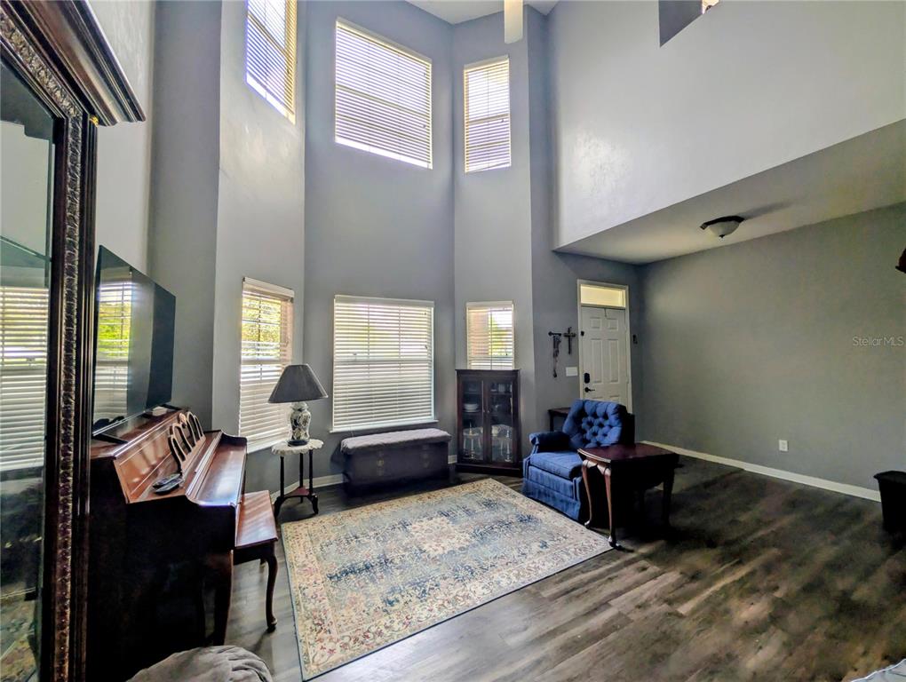 A living room with high ceilings, large windows, a piano, and wood-look flooring — 2717 NW 103RD WAY UNIT O, GAINESVILLE, FL