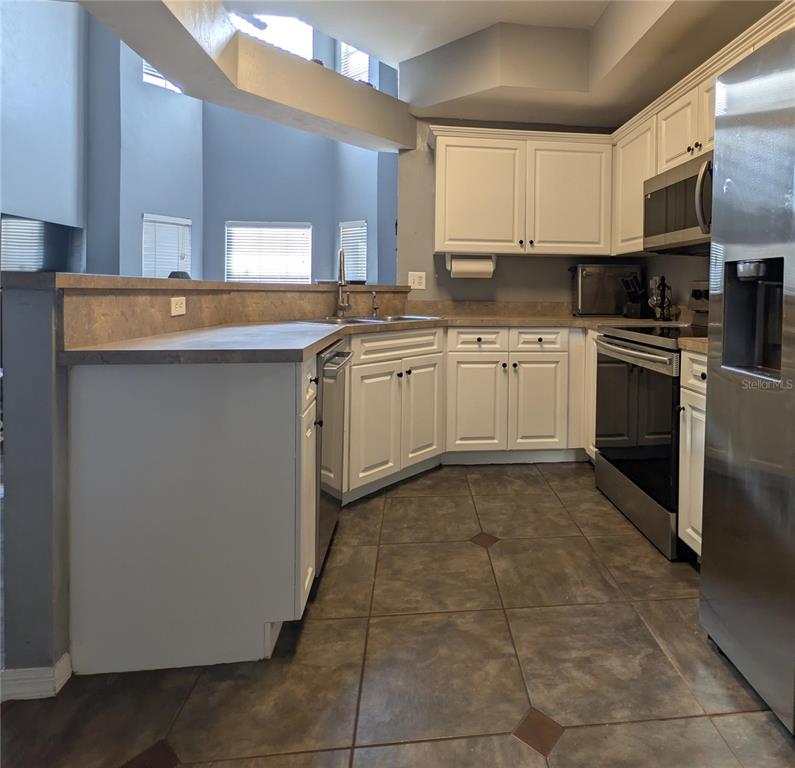 A kitchen features white cabinets, stainless steel appliances, and dark tile flooring — 2717 NW 103RD WAY UNIT O, GAINESVILLE, FL