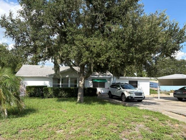 A white single-story house with a large oak tree and a carport in the front yard — 964 OHLINGER ROAD, BABSON PARK, FL