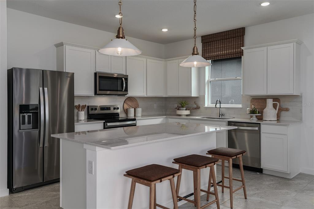 A modern kitchen features white cabinets, stainless steel appliances, a quartz island, and three stools — 8545 SW 65TH STREET ROAD, OCALA, FL