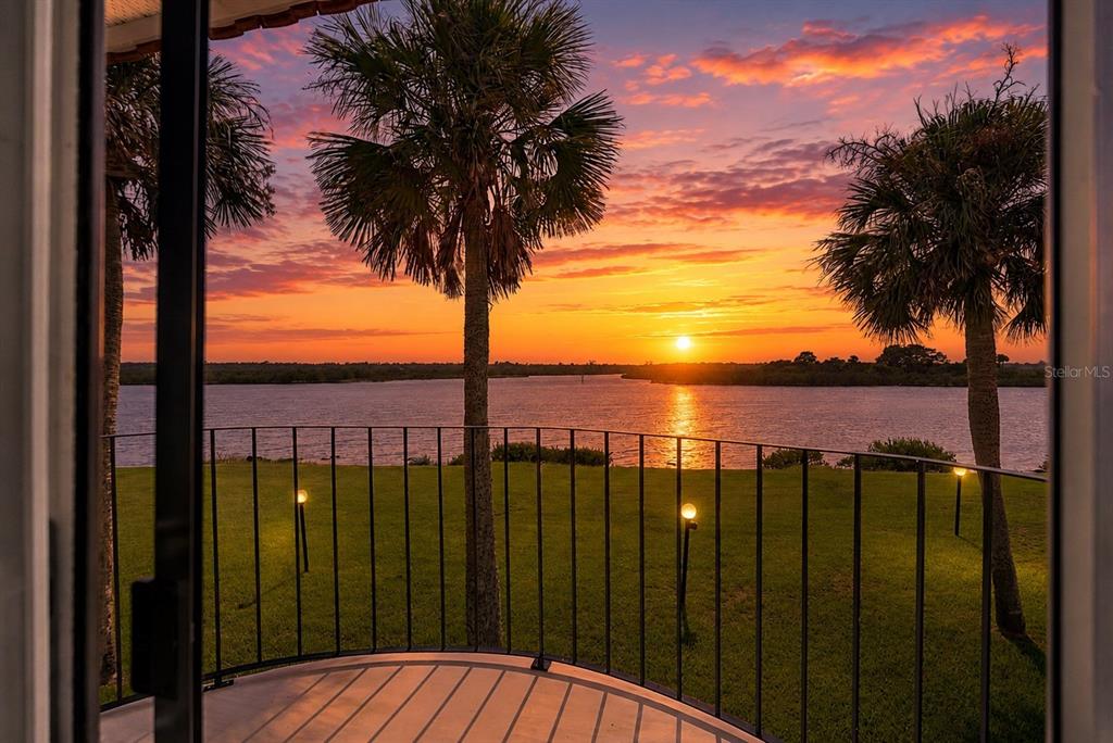 A balcony with a metal railing overlooks a grassy lawn, palm trees, and a sunset — 51 S OCEAN PALM DRIVE, FLAGLER BEACH, FL