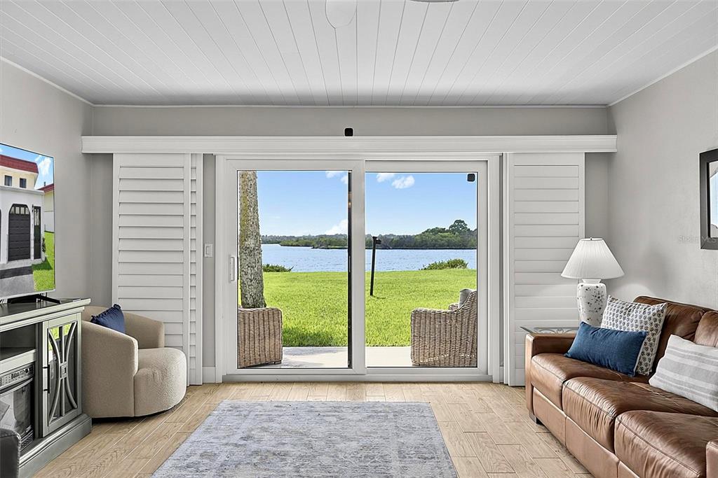 A living room with wood-look tile floors, a leather sofa, and sliding doors overlooking water — 51 S OCEAN PALM DRIVE, FLAGLER BEACH, FL
