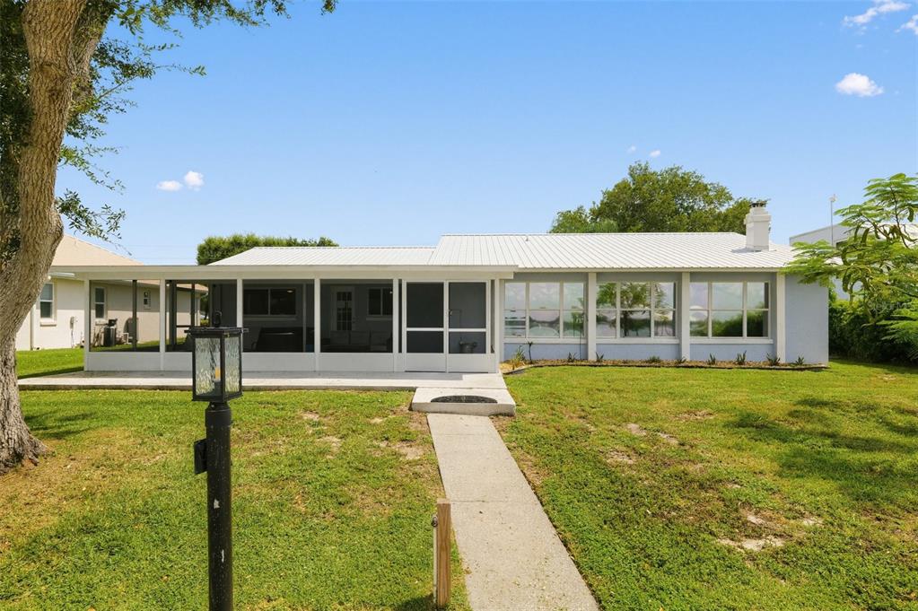 A light blue house with a metal roof and large windows sits on a grassy lawn — 186 MANDOLIN DRIVE, LAKE PLACID, FL
