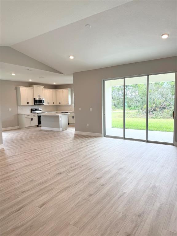 A living room with light wood floors, a grey sofa, and an open kitchen area — 5336 COLUMBUS BOULEVARD, SEBRING, FL