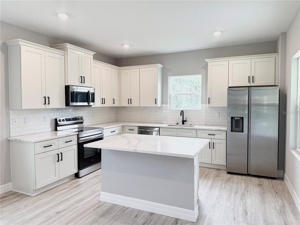 A modern kitchen features white cabinetry, stainless steel appliances, a center island, and light flooring — 5336 COLUMBUS BOULEVARD, SEBRING, FL