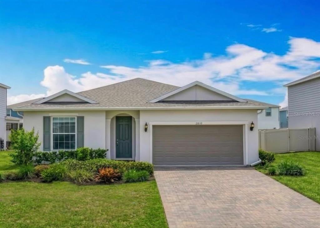 The exterior of a house features a dark green front door, a garage, and landscaping — 2610 HILLTOP LOOP, APOPKA, FL