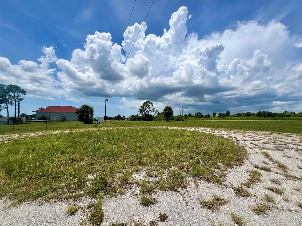 A grassy, partially paved lot under a large, cloudy blue sky — 32 TEAK LANE, PLACIDA, FL