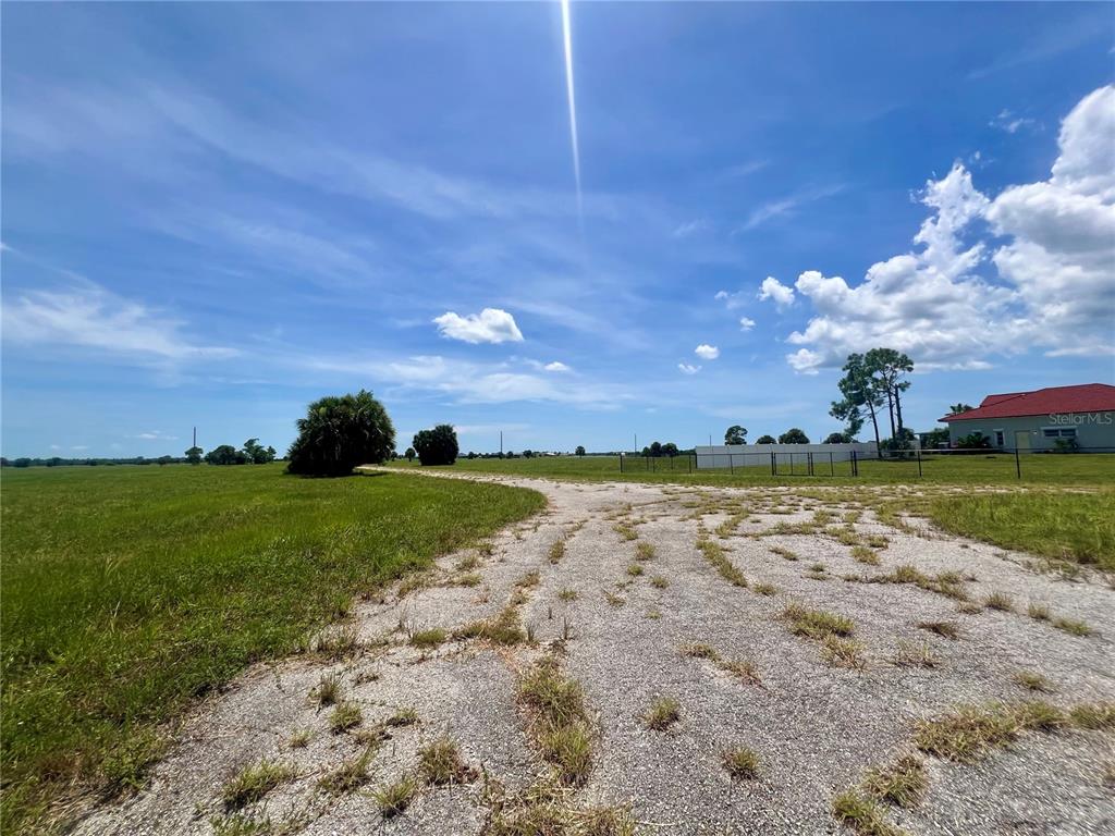 A gravel driveway leads through a grassy field toward a house under a blue sky — 32 TEAK LANE, PLACIDA, FL