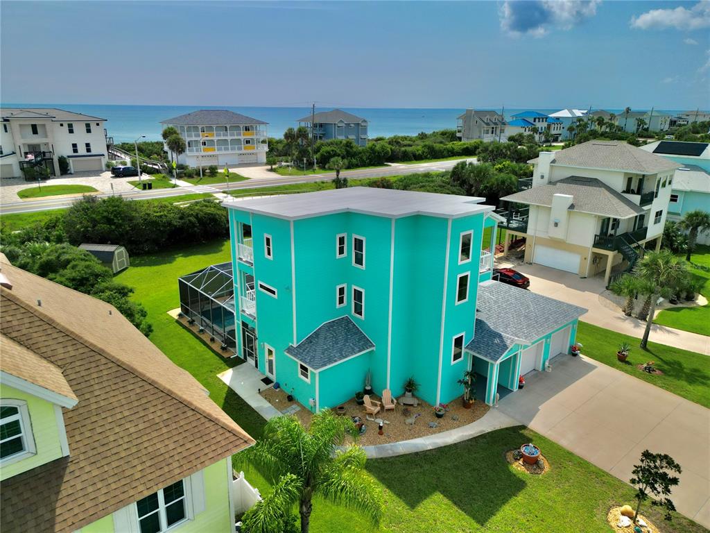 An aerial view shows a bright turquoise three-story house with a pool and attached garage — 3073 PAINTERS WALK, FLAGLER BEACH, FL