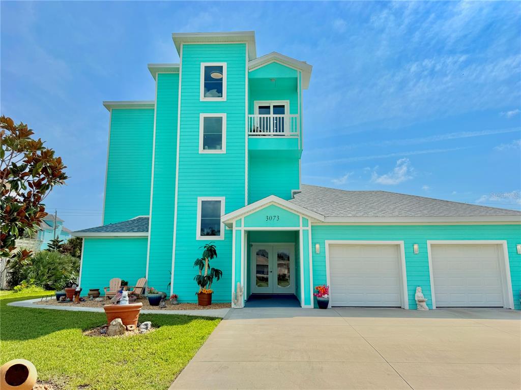 A bright turquoise three-story house with a two-car garage and a small front balcony — 3073 PAINTERS WALK, FLAGLER BEACH, FL