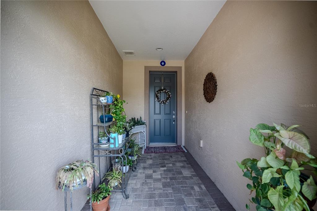 A covered entryway features a dark blue front door, a metal plant stand, and potted plants — 9145 SW 70TH LOOP, OCALA, FL