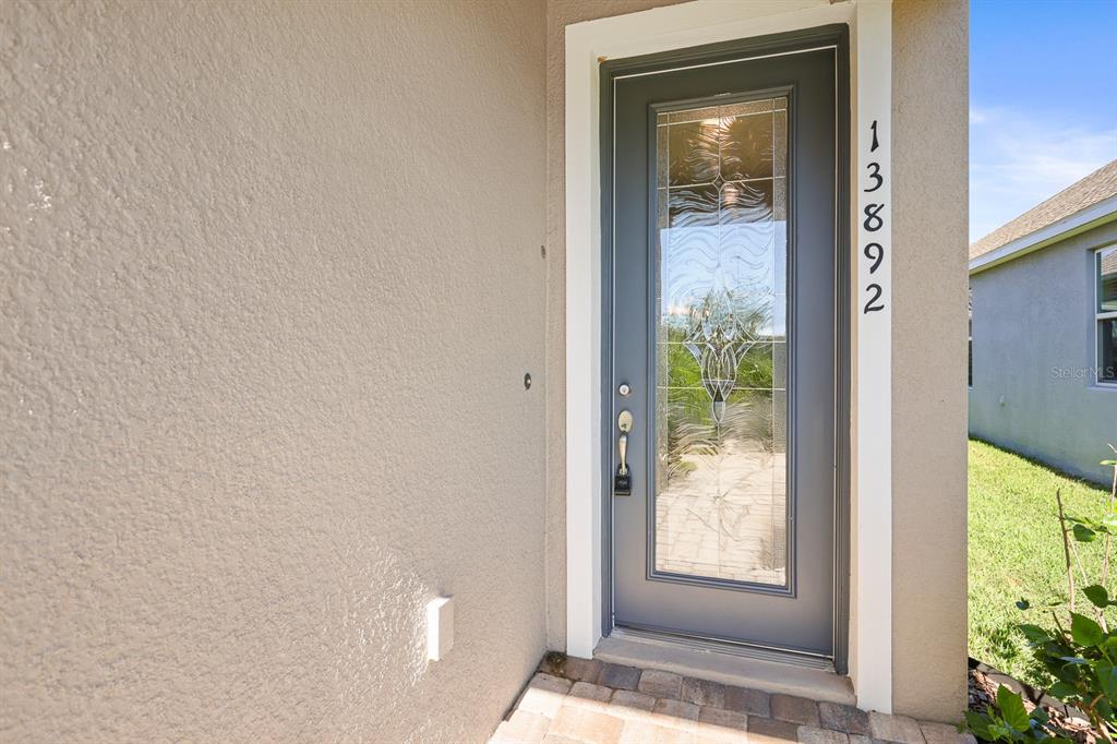 A gray front door with a decorative glass insert is set in a stucco wall — 13892 KINGFISHER GLEN DRIVE, LITHIA, FL