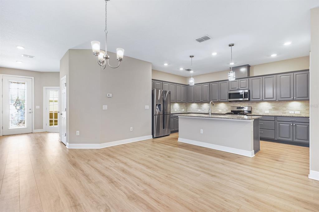 A kitchen with gray cabinets, stainless steel appliances, and an island opens to a dining area — 13892 KINGFISHER GLEN DRIVE, LITHIA, FL
