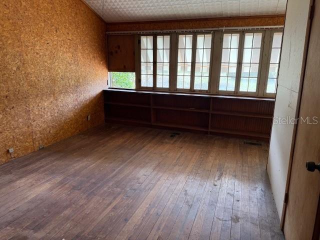 A room with wood-paneled walls, hardwood floors, and a long built-in wooden bookshelf under windows — 1600 E LAKEVIEW AVENUE, EUSTIS, FL