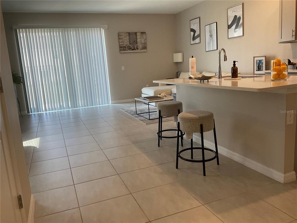 A kitchen island with two stools overlooks a living area with tile flooring — 7633 WATERSCAPE DRIVE, GROVELAND, FL
