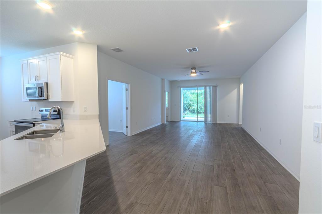 A modern kitchen with white cabinets and a quartz island opens into a spacious living area — 407 THREE OAKS DRIVE, EDGEWATER, FL