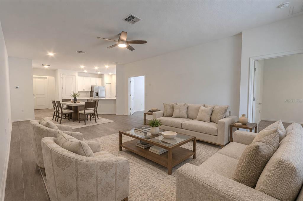 An empty room with gray wood-look tile flooring and white walls, leading into a kitchen — 407 THREE OAKS DRIVE, EDGEWATER, FL